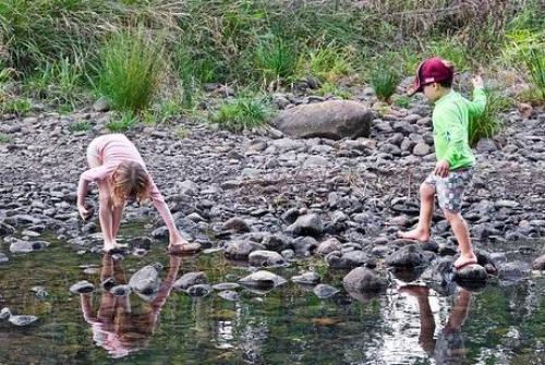 Two children playing by a shallow rocky stream. One of the children is walking across stepping stones.