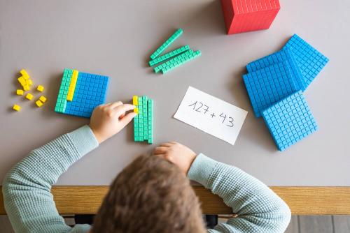 Overhead picture of a boy working with base ten blocks to calculate 127+43.