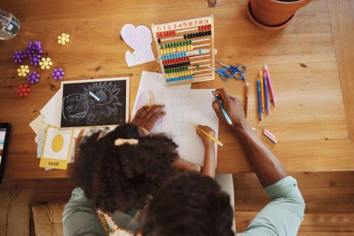 Overhead picture of a girl and adult doing maths together on a desk.